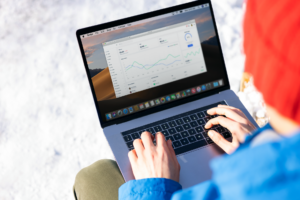Une personne en veste bleue analysant des analyses commerciales sur un ordinateur portable en extérieur en hiver.