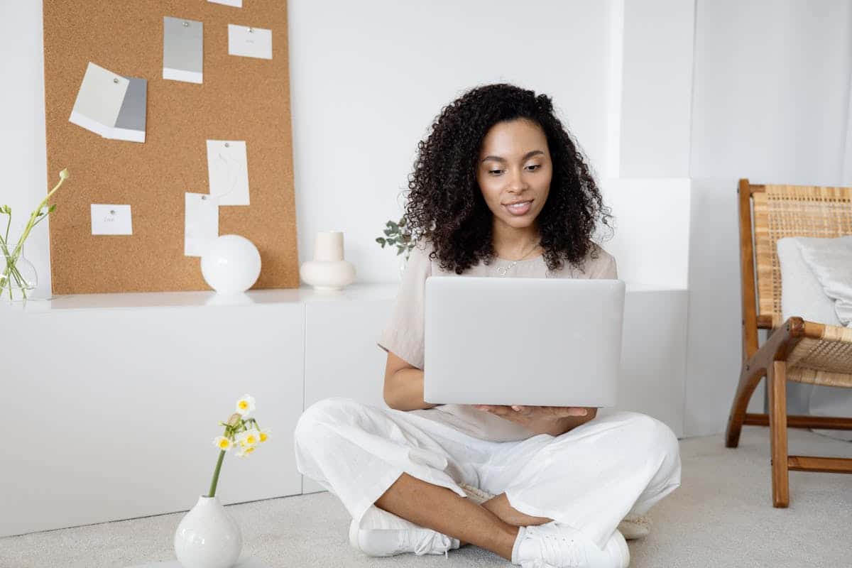 Logiciel de gestion hôtelière : efficacité et satisfaction des clients réunies Young woman with curly hair working on her laptop in a cozy home setting, exuding confidence and focus.