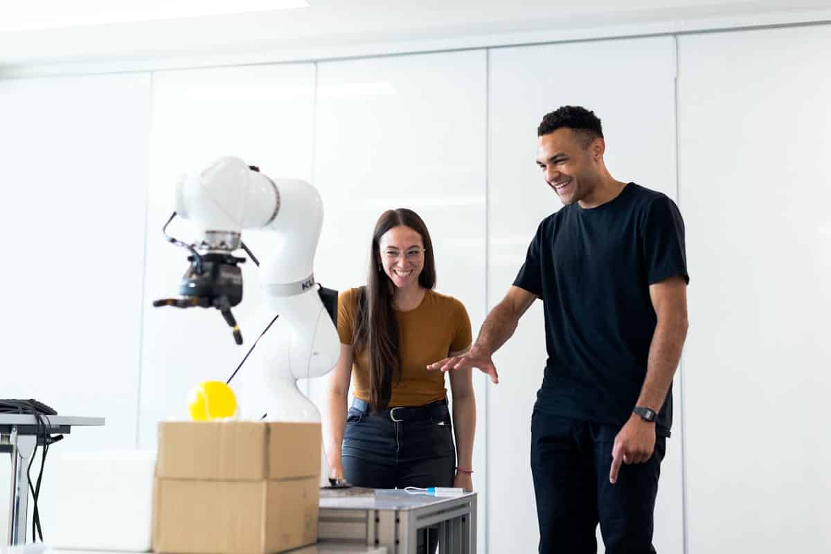 Les robots comme collègues : qu’advient-il du travail d’équipe lorsque l’IA devient un membre à part entière d’un projet? Two engineers collaborating on testing a futuristic robotic prototype in a modern indoor lab.