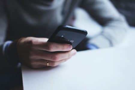 La téléphonie fixe moderne sans internet : une solution simple et fiable avec Bleufix Close-up of a person holding a smartphone while sitting at a white table.