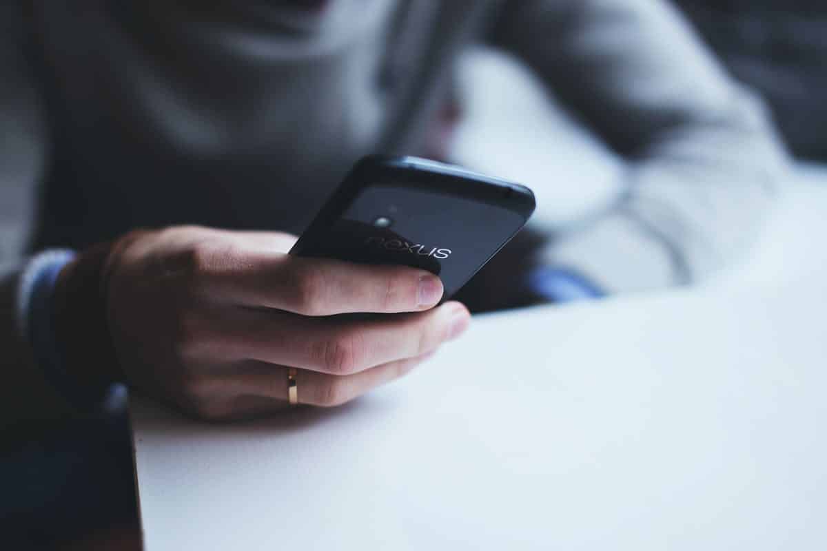 La téléphonie fixe moderne sans internet : une solution simple et fiable avec Bleufix Close-up of a person holding a smartphone while sitting at a white table.