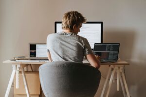 Le rôle croissant des API dans le développement web moderne Young man coding at home office with multiple laptops, representing remote work and technology.