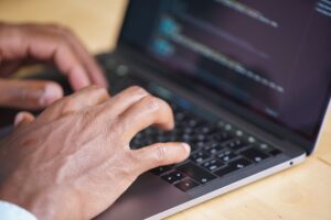 Développer des solutions sur-mesure : avantages et inconvénients Hands typing on a laptop with code displayed on screen, showcasing technology use.
