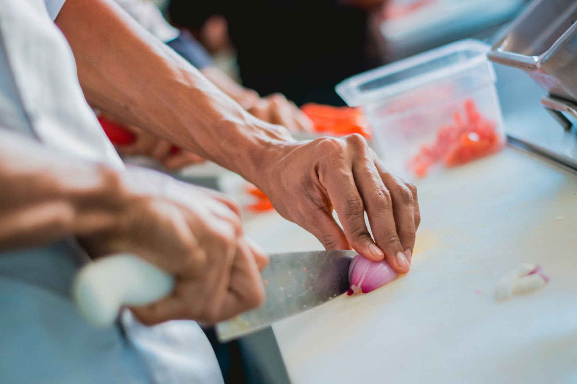 Gros plan d'un chef coupant un oignon dans une cuisine, mettant l'accent sur la préparation des aliments.