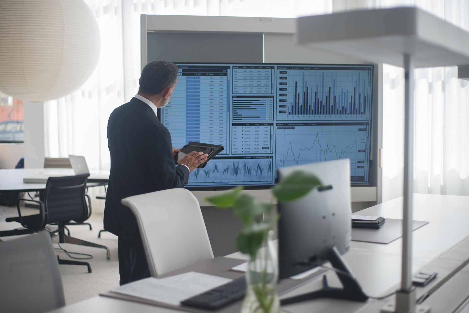 Professionnel en costume analysant des données financières sur des écrans dans un bureau moderne.