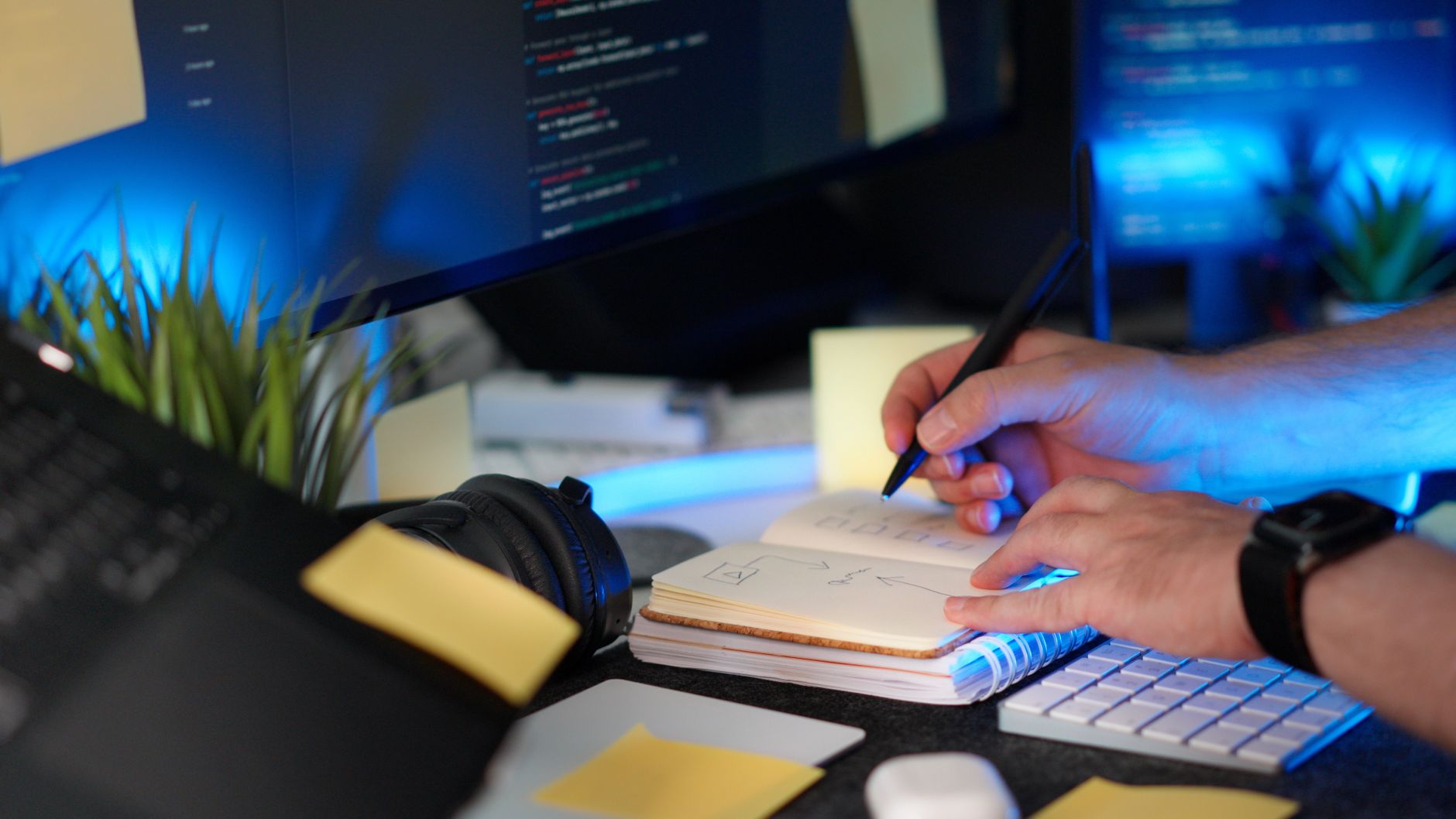 Une personne planifie un projet logiciel avec des notes manuscrites et du code sur un moniteur dans un espace de travail moderne.
