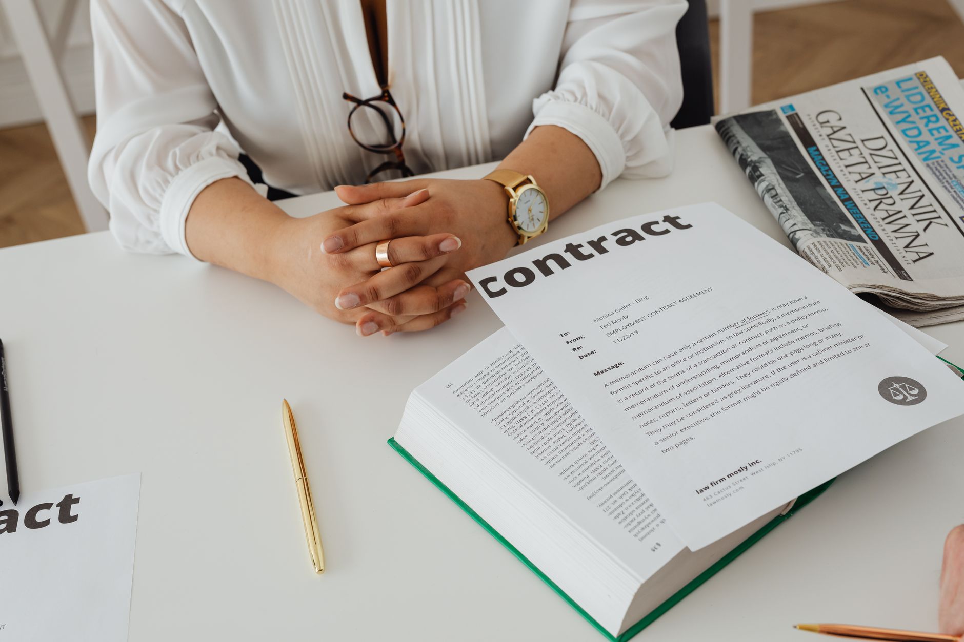 Femme d'affaires assise à son bureau examinant un contrat avec des documents juridiques et un journal.