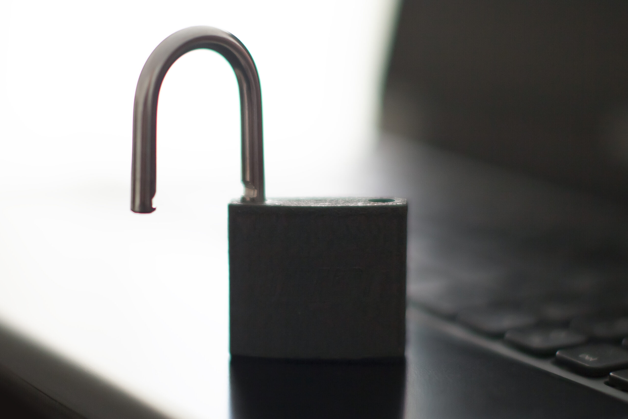 Cadenas ouvert posé devant le clavier flou d’un ordinateur portable noir.